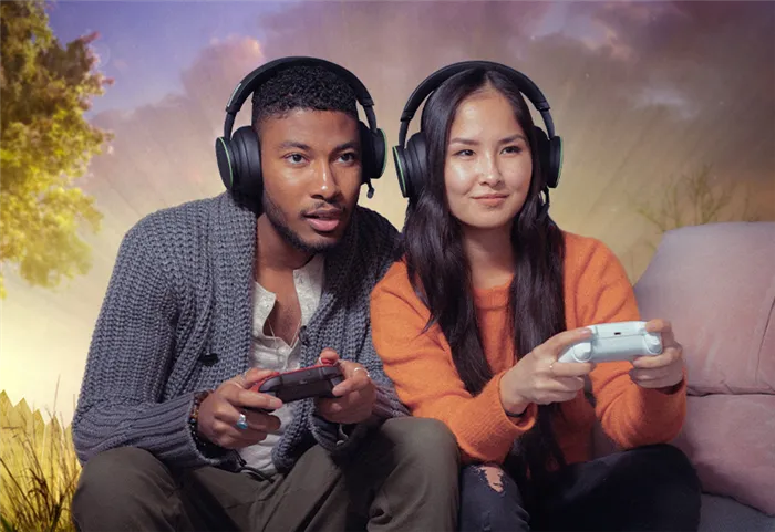 Два человека в наушниках и вместе играют в игры Xbox на диване.