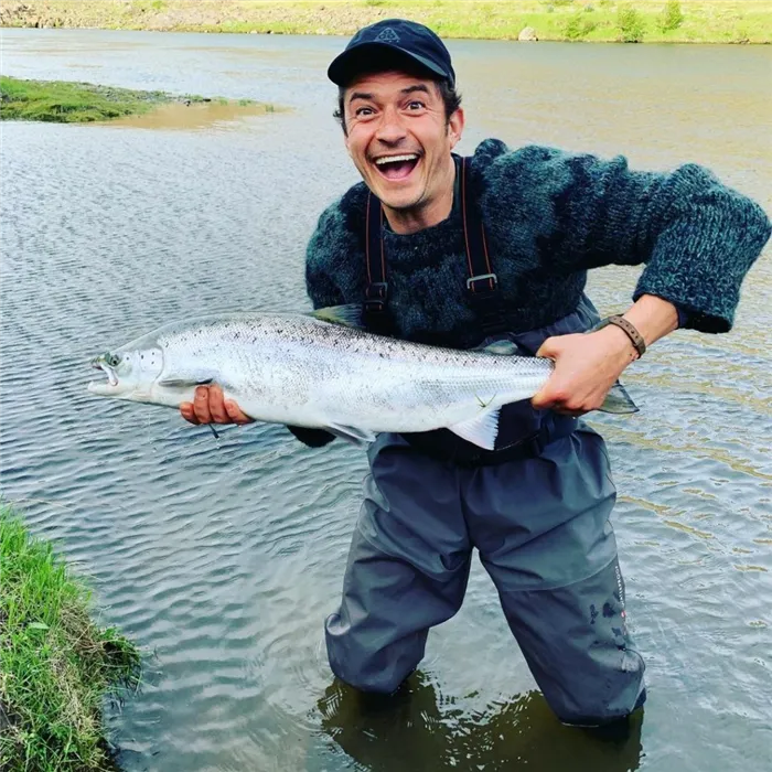 Актер Орландо Блум на рыбалке. У него в руке большая рыба.